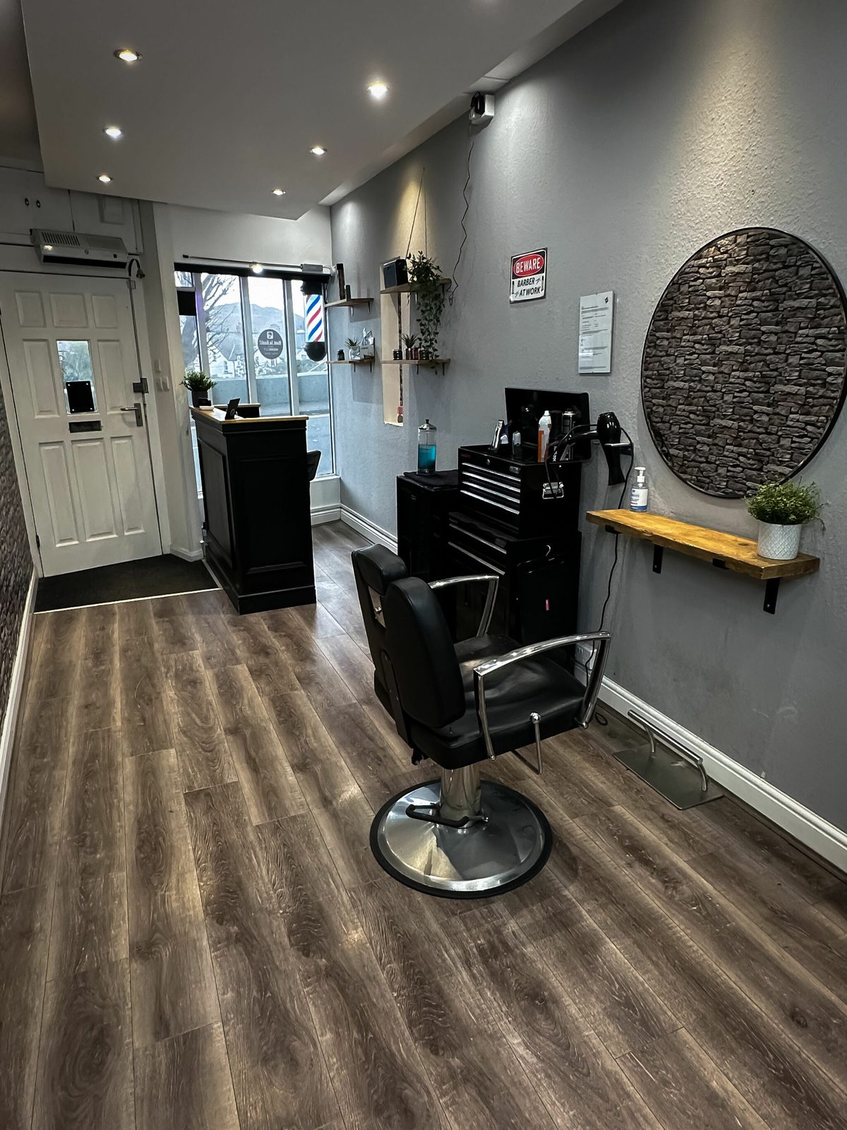 Black barber chair facing the glass entrance and barber pole on Station Road
