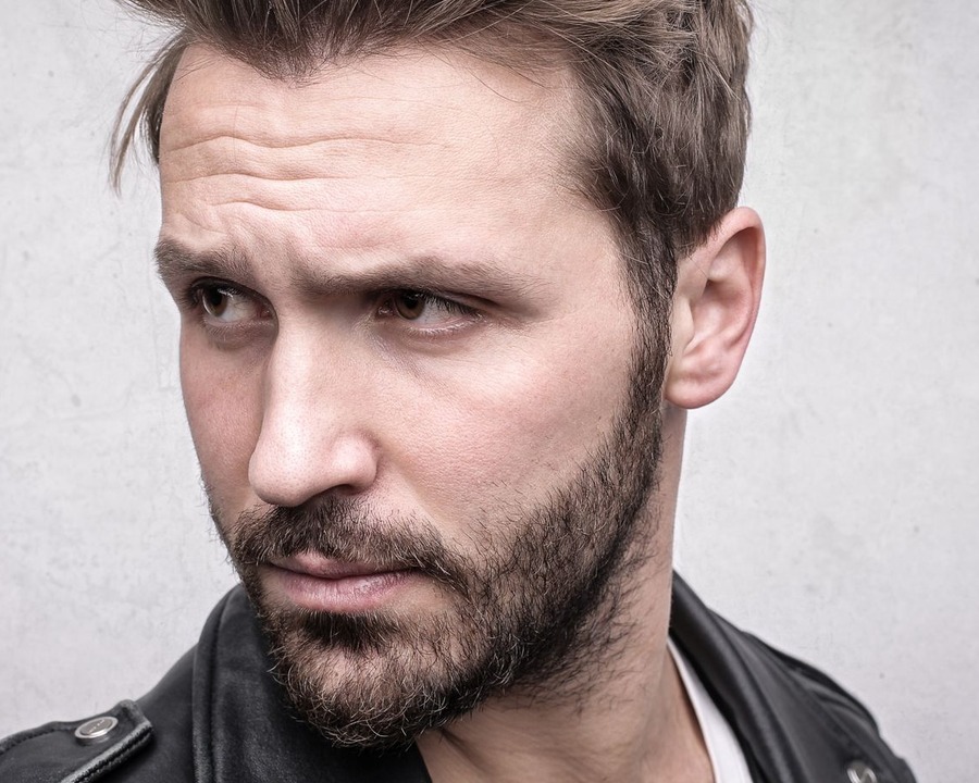 Close portrait of a white British-looking man with a neat short beard and textured short back and sides cut with visible length on the sides