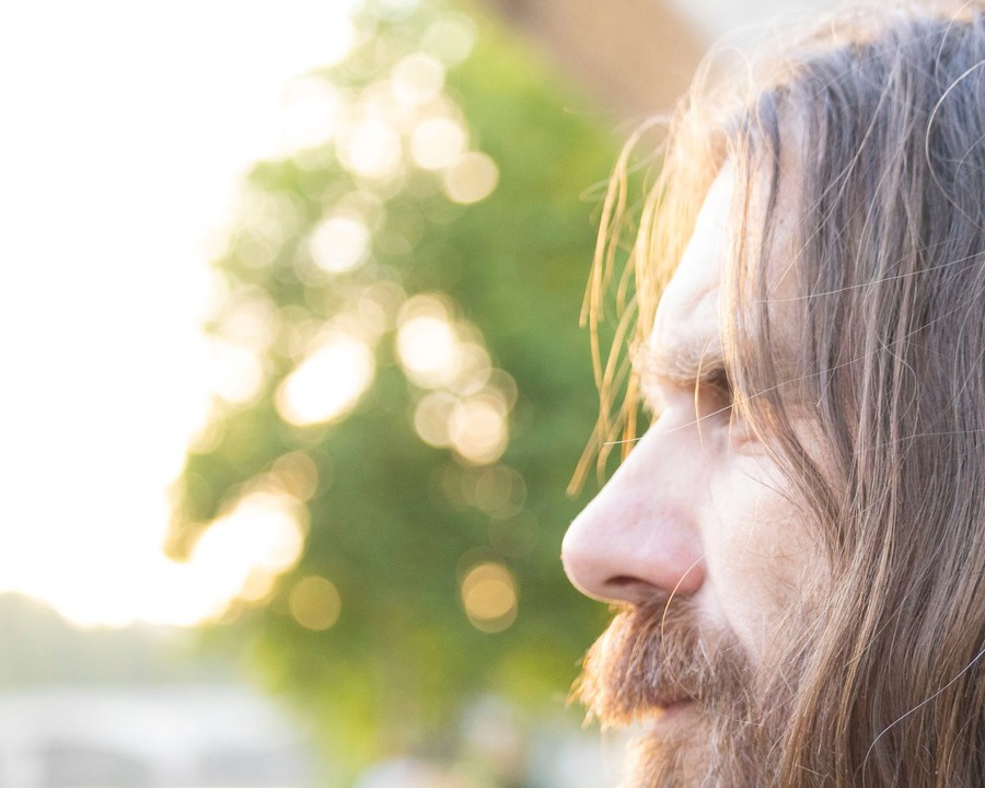 Side profile of a white British-looking man with longer layered hair past the ears